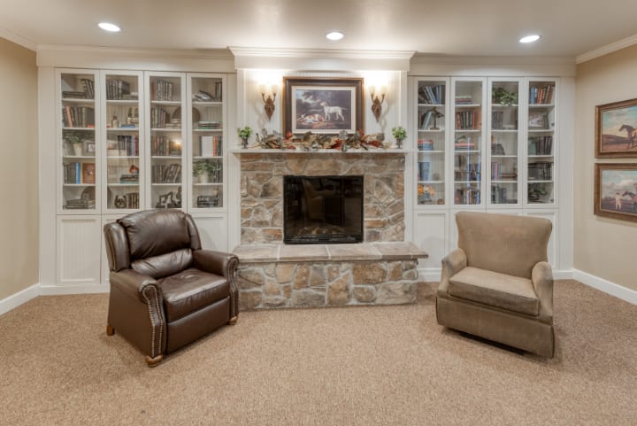 A cozy living room featuring a stone fireplace flanked by glass-fronted bookshelves and comfortable armchairs.