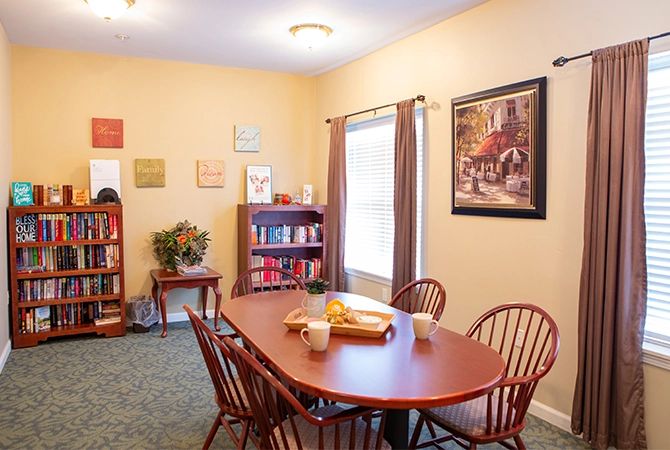 A cozy dining room with a wooden table, surrounded by chairs, a bookshelf with books, and artwork on the walls.