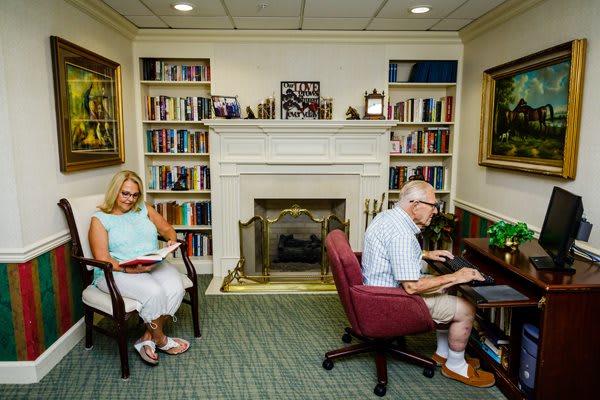 Two people reading in a cozy library with a fireplace.