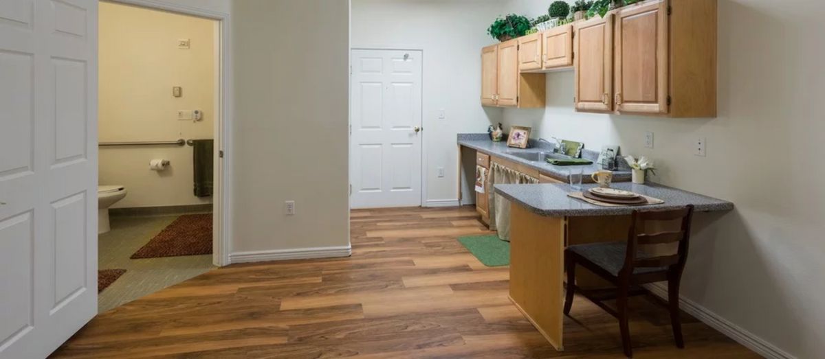 A modern kitchen with wooden flooring, light-colored cabinets, and a sleek countertop.