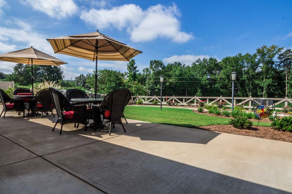A sunny patio with a table and chairs under an umbrella, overlooking a well-maintained garden.