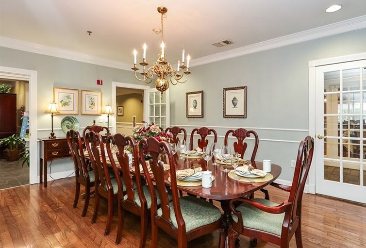 An elegant dining room with a long wooden table set for dinner, featuring a chandelier overhead and decorative wall art.