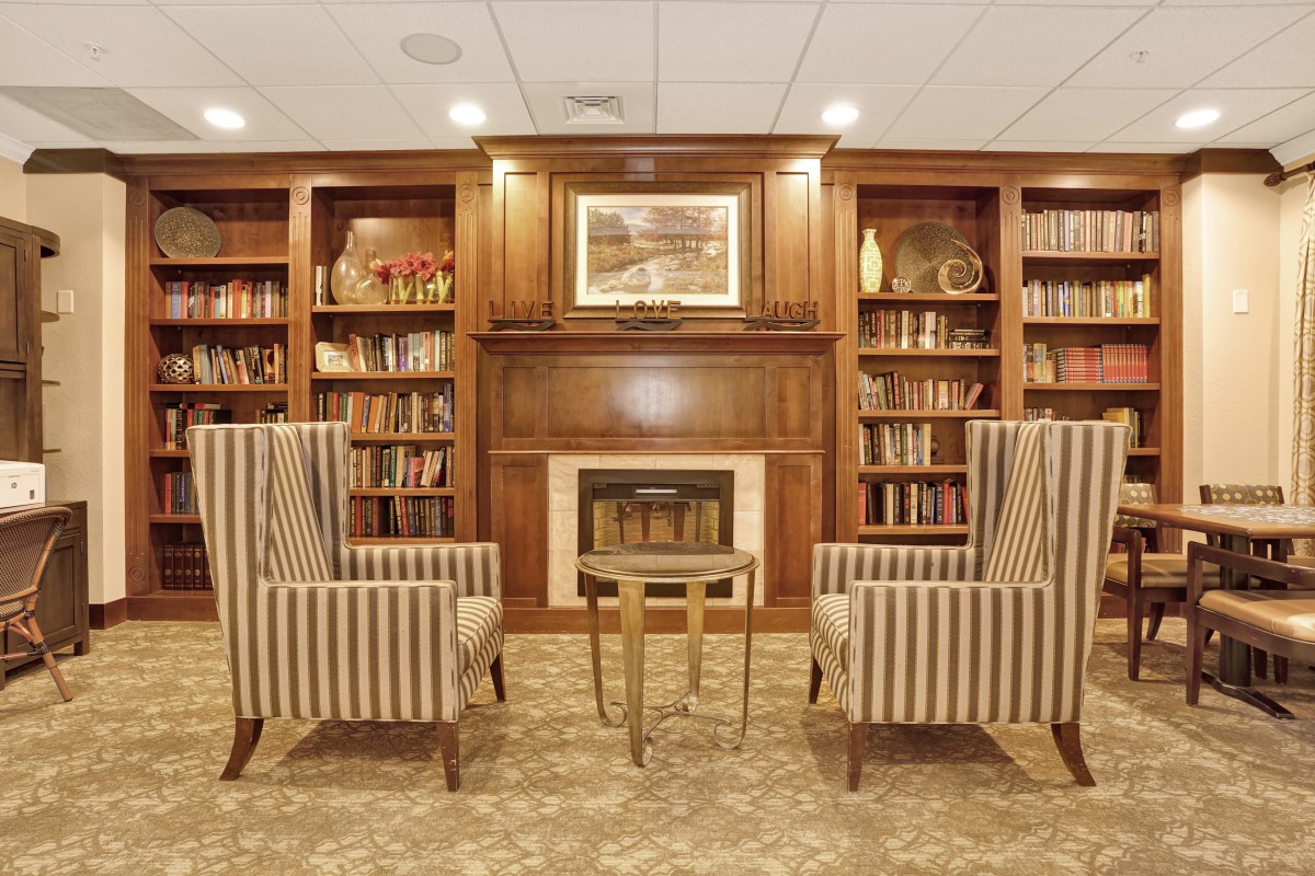 A cozy library interior with bookshelves, a fireplace, and striped armchairs.