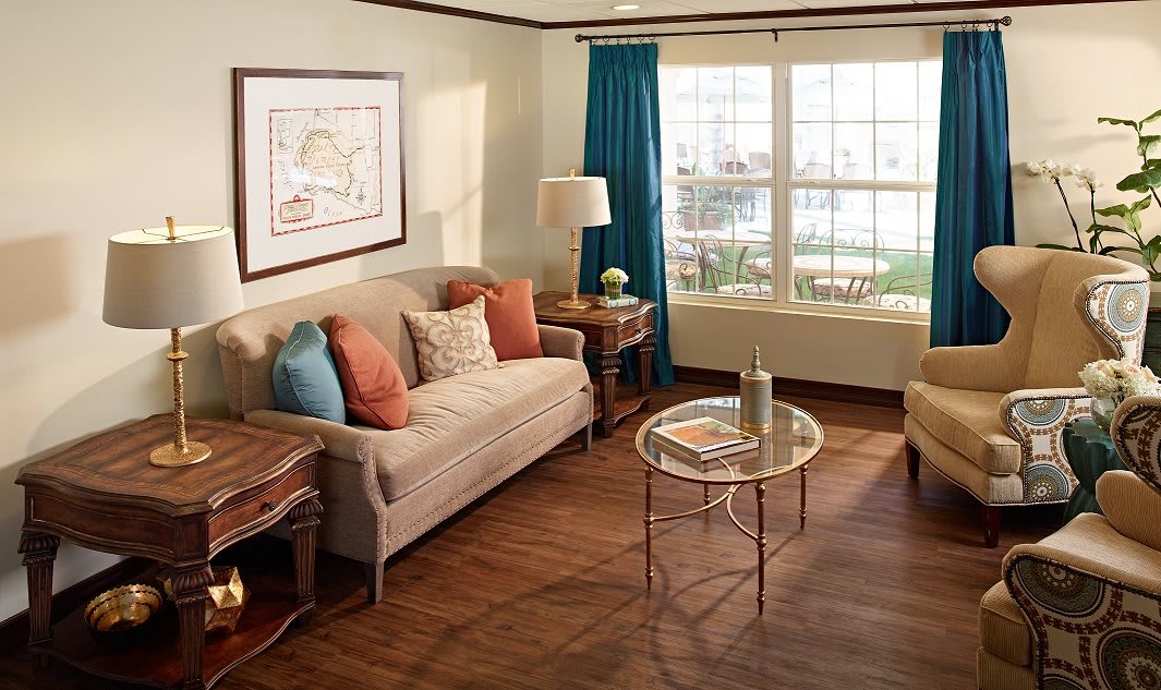 A cozy living room with a sofa, glass coffee table, and large window draped with blue curtains.