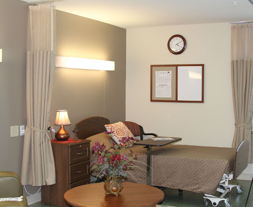 A well-lit hospital room featuring a bed, bedside lamp, and a small table with a flower vase.