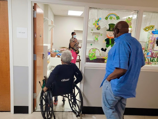 A visitor observing a patient in a wheelchair being attended to by medical staff in a healthcare facility.