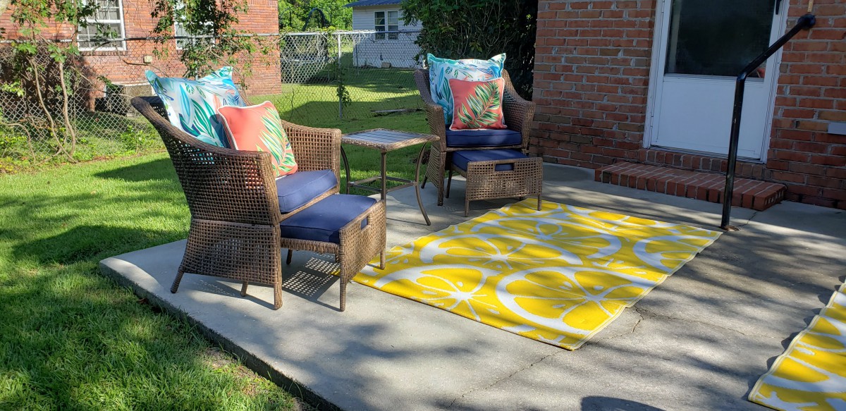 A cozy outdoor patio with wicker chairs, colorful cushions, and a bright yellow rug.