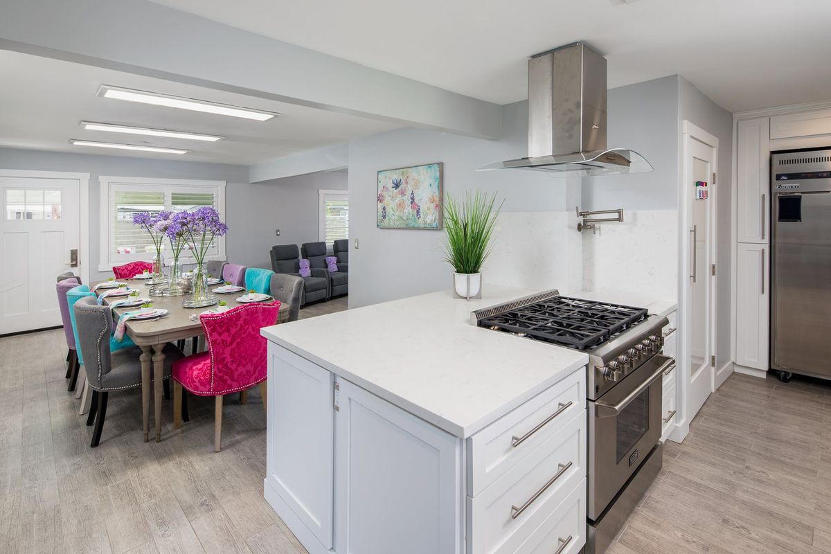A modern kitchen with a sleek design, featuring a stove and range hood, a white countertop, and a colorful dining area.