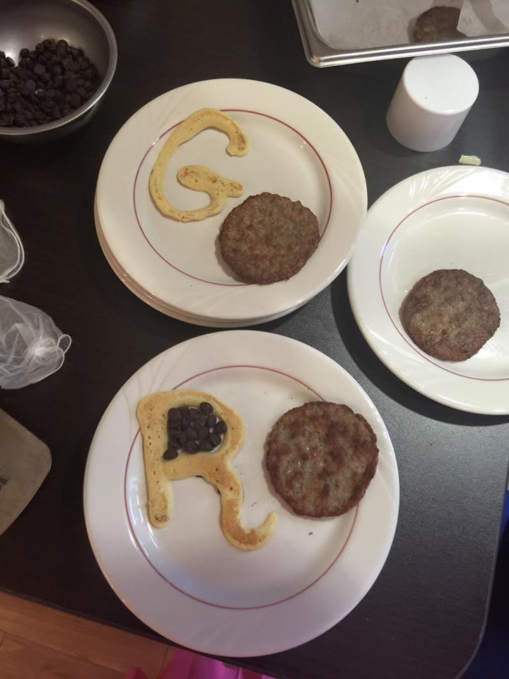 Plates with burger patties and pancake letters arranged in a creative display.