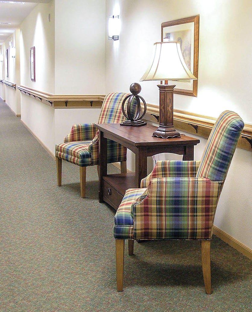 A hallway with plaid upholstered chairs and a wooden table, adorned with a decorative lamp.