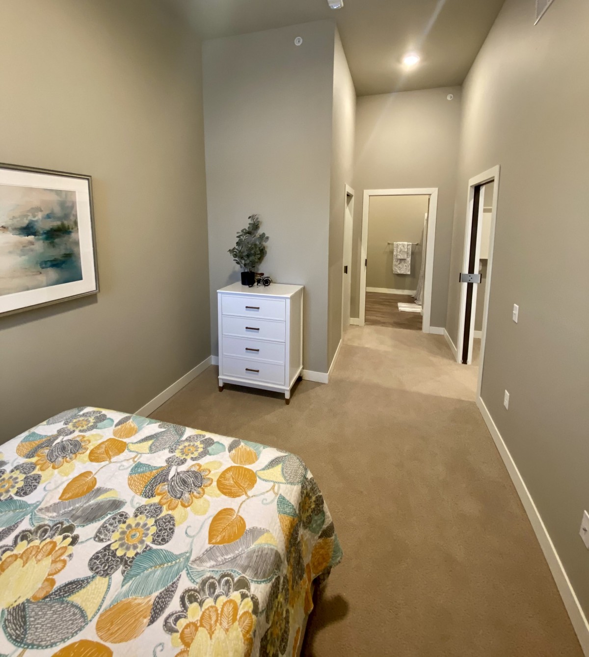 A modern bedroom with a floral bedspread, dresser, and wall art.