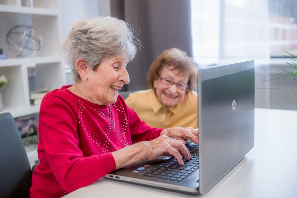 Two elderly women smiling while using a laptop together.