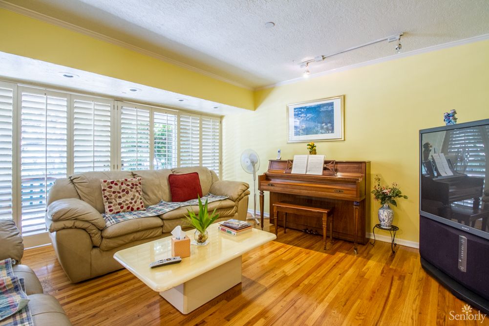 A cozy living room with a sofa, piano, and coffee table on a hardwood floor.