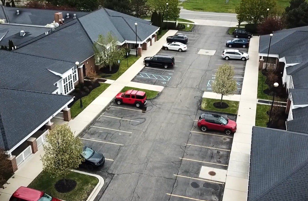 Aerial view of a parking lot next to residential buildings, featuring several parked cars.