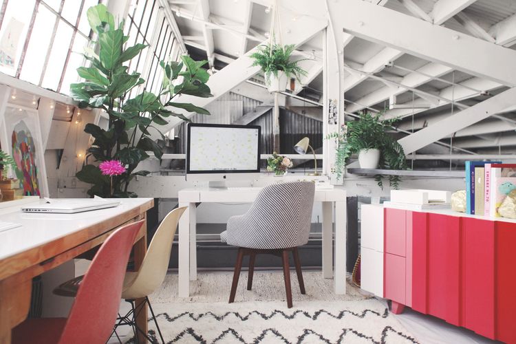 A stylish and cozy home office setup with a computer desk surrounded by lush green plants.