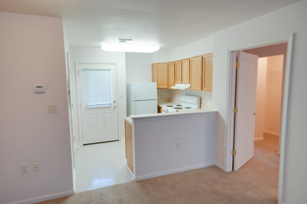 View of a compact apartment kitchen with light wooden cabinets and white appliances.