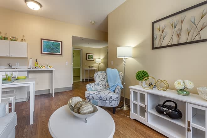 A cozy living room with a patterned armchair, a side table, decorative items, and wall art.
