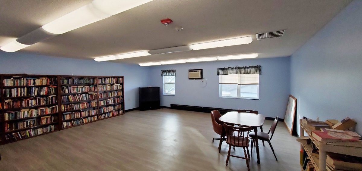 A cozy library reading room with bookshelves, tables, and chairs by the windows.