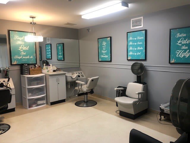 A salon interior featuring styling chairs, a mirror, hair drying station, and decorative posters on the walls.
