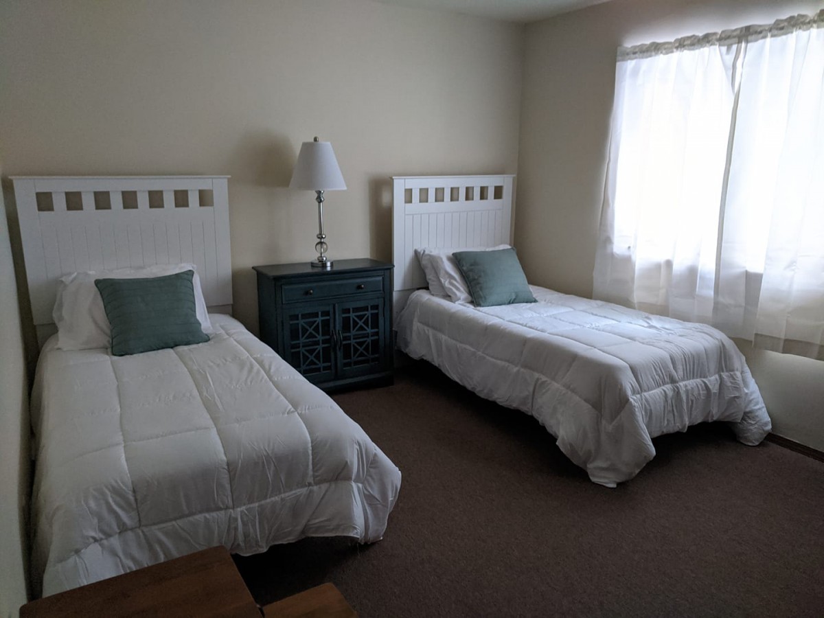 A simple bedroom featuring two twin beds with white bedding and a lamp between them.