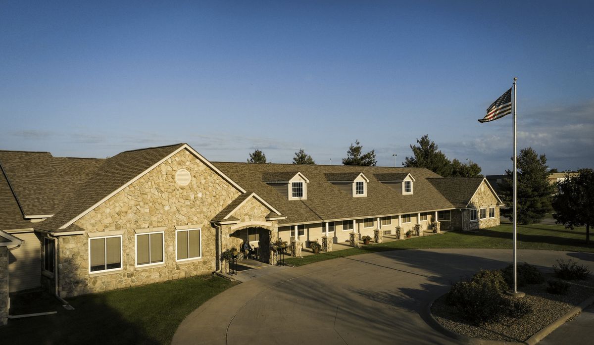 A stone residential building with a series of dormer windows and an adjoining driveway under a clear blue sky.