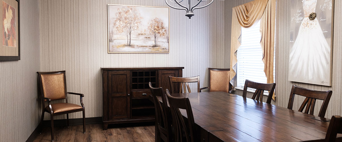 A cozy dining room with a wooden table, chairs, and a cabinet, adorned with wall art and a chandelier.