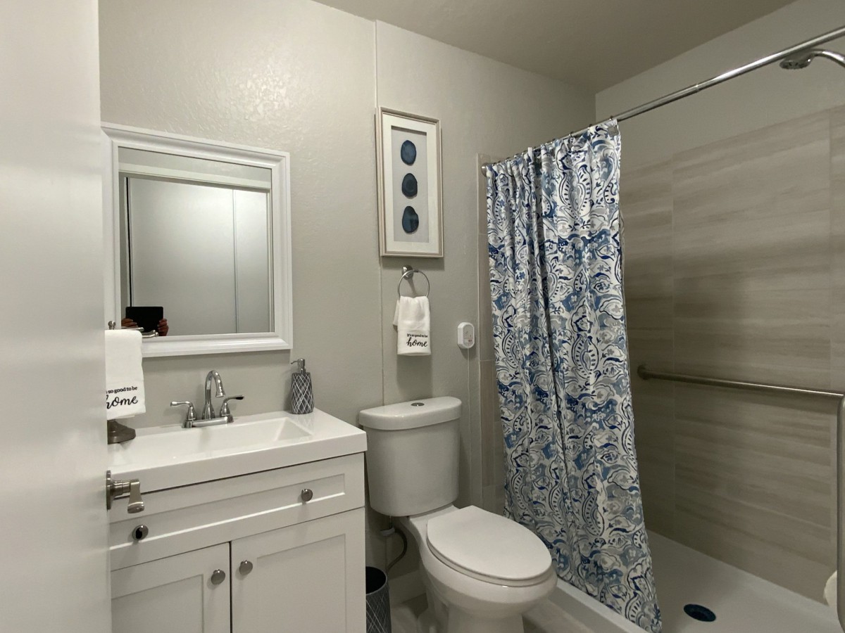A modern bathroom with a white sink, mirror, toilet, and a blue patterned shower curtain.