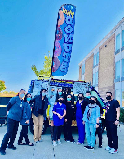 A lively group gathers in front of a colorful donut food truck at a community event.