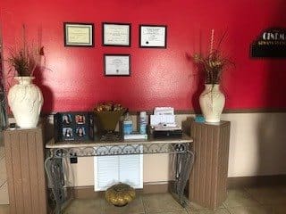 A waiting area with a decorative console table, certificates on the red wall, and vases on pedestals.