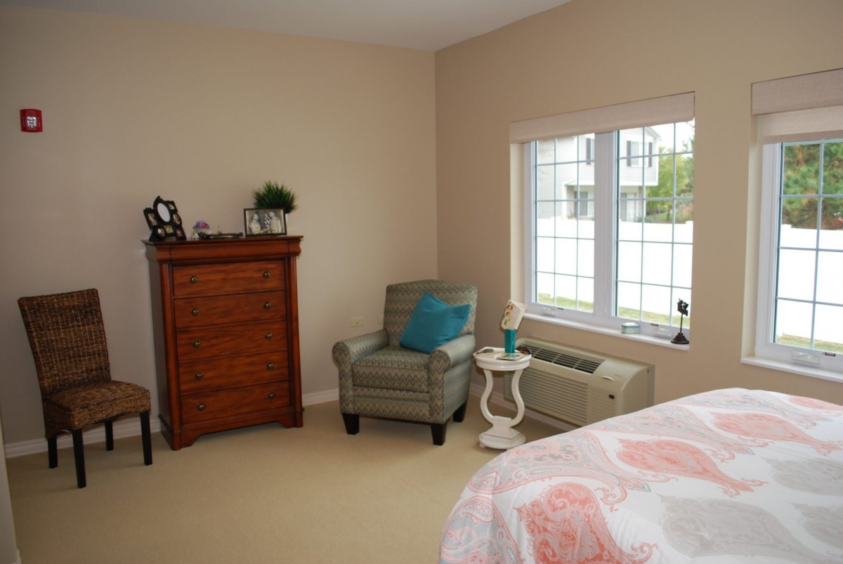 A cozy bedroom corner with a chair, dresser, and a bright window.