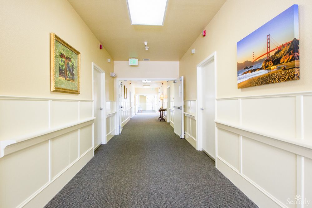 A well-lit, carpeted hallway with artwork on the walls and several doors leading to different rooms.