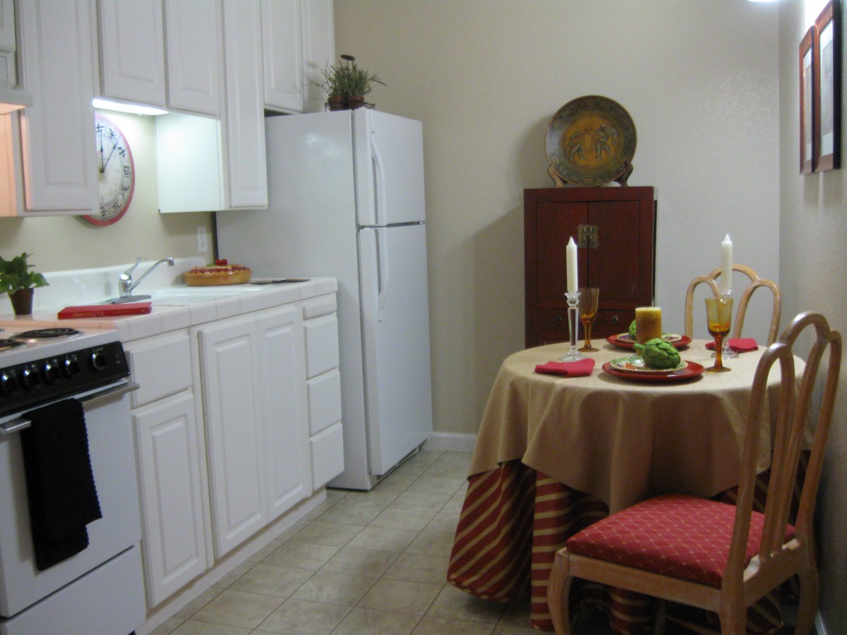 A cozy kitchen and dining area with a small round table set for a meal, featuring candles and decorative elements.
