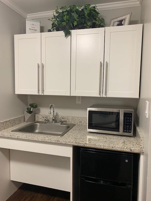 A compact kitchen area with white cabinets, a sink, a microwave, and a mini fridge.