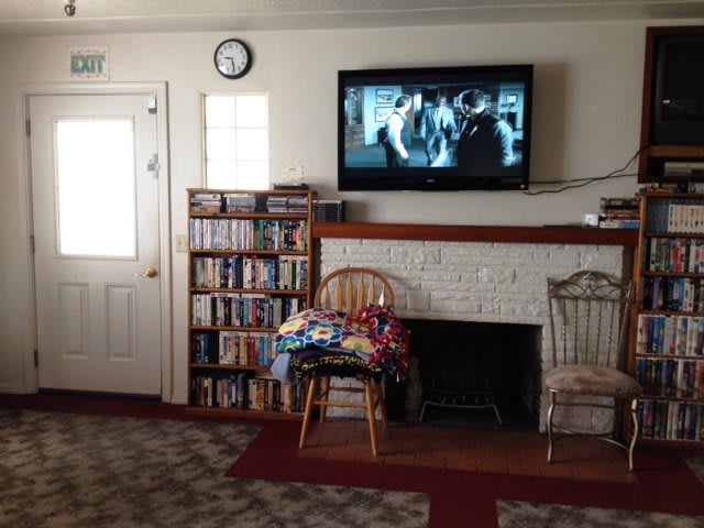 A cozy living room with a television mounted above a fireplace, flanked by a bookshelf and two chairs.