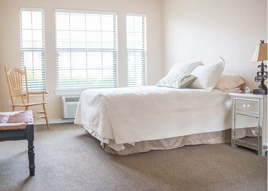 A bright and minimalist bedroom with white bedding and large windows letting in natural light.