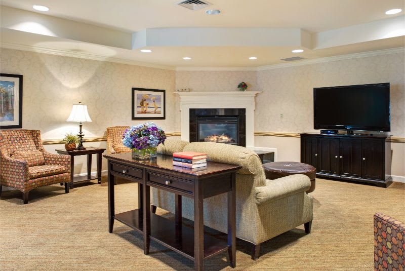 A cozy living room featuring a fireplace, sofa, television, and coffee table with books and flowers.