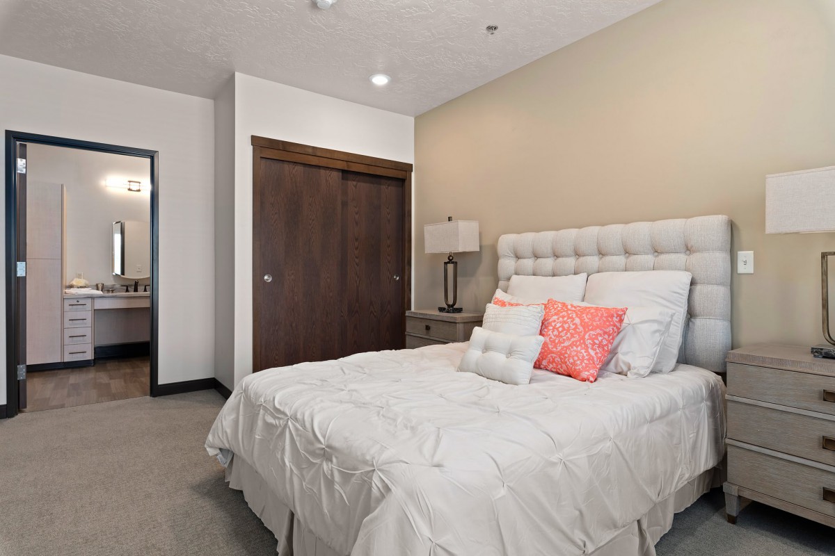 A cozy bedroom featuring a neatly made bed with decorative pillows, a bedside lamp, and a closet door.