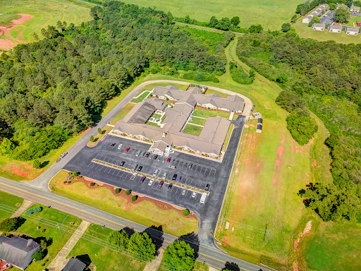 Aerial view of a building surrounded by lush greenery and a spacious parking lot.