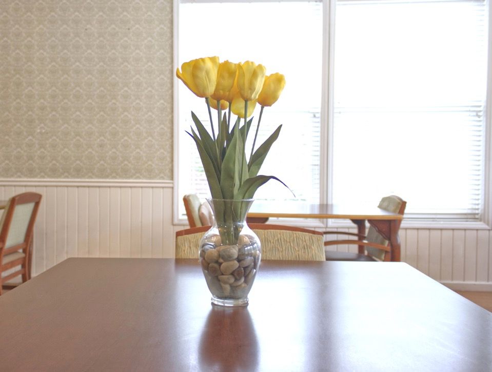 A vase of yellow tulips on a wooden table, illuminated by natural light from a window.
