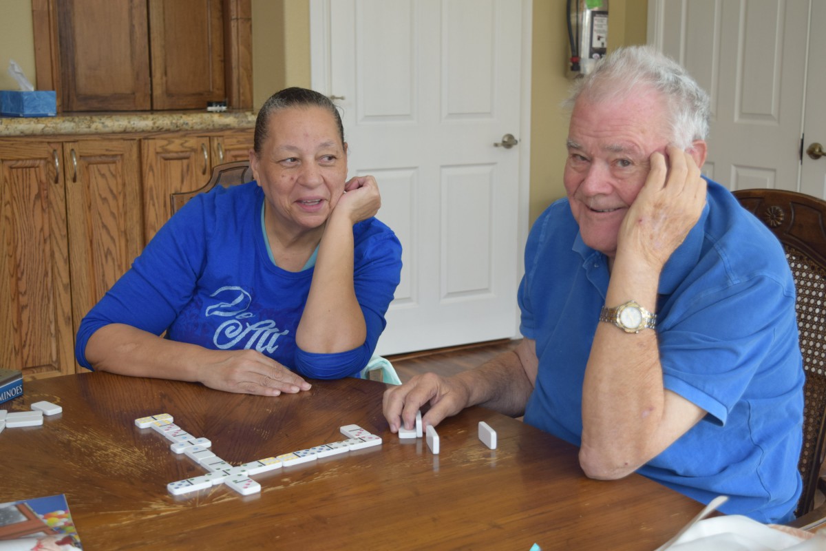 A smiling elderly couple enjoying a game of dominoes together at a table.