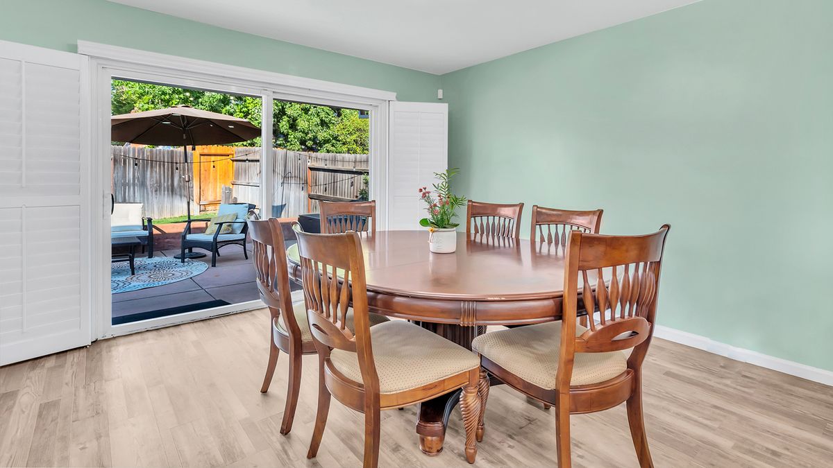 A cozy dining room with a wooden table and chairs, featuring a potted plant centerpiece and sliding doors leading to an outdoor patio.