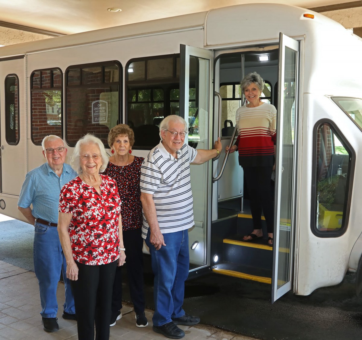 A group of seniors standing beside a bus, with one person stepping inside.