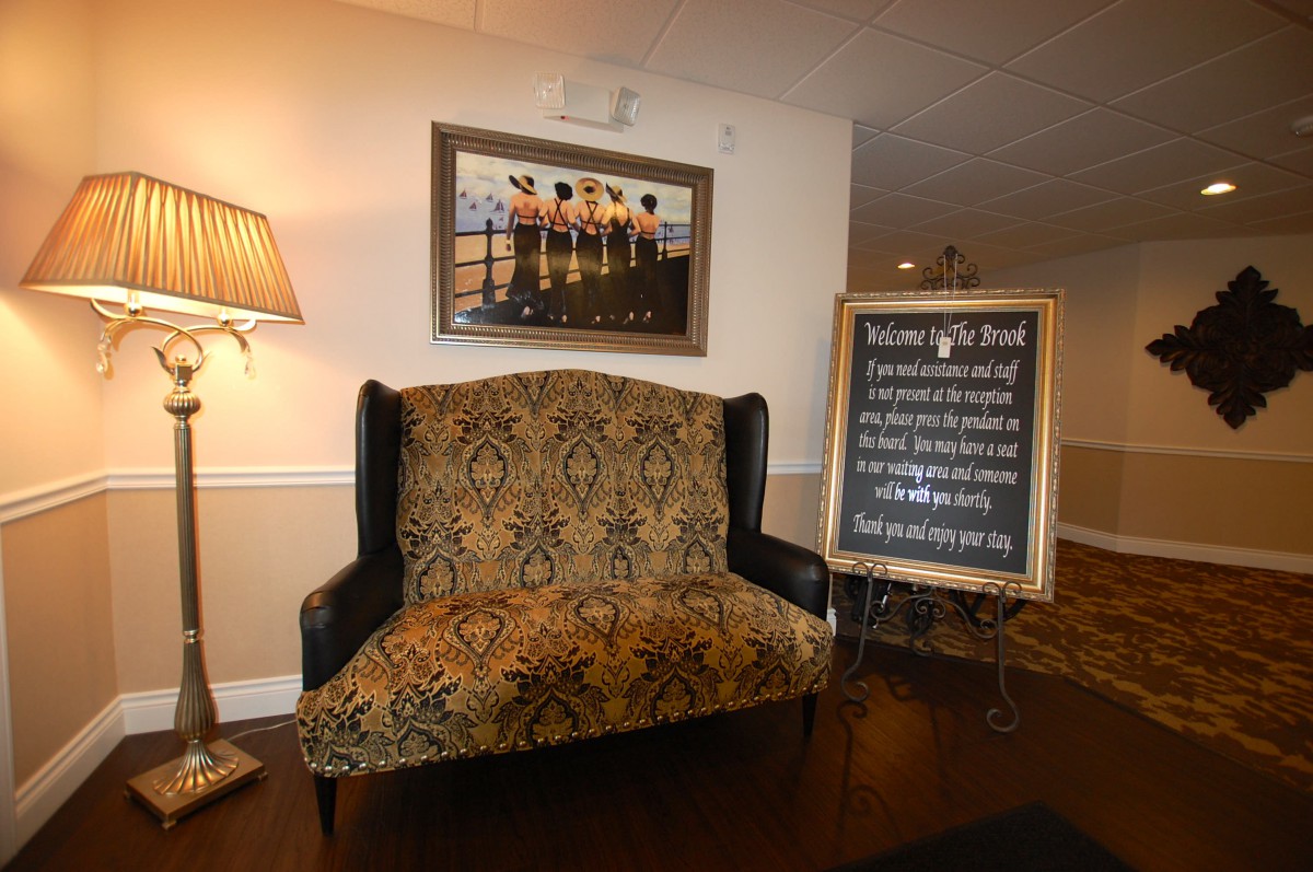 A cozy seating area with a patterned bench, a lamp, wall art, and a signboard displaying information.