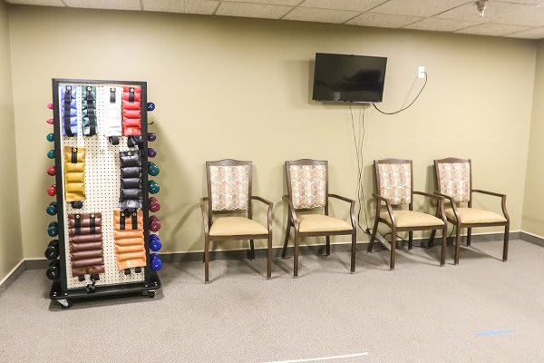 A waiting area with lined-up chairs, a wall-mounted television, and a rack of exercise equipment.