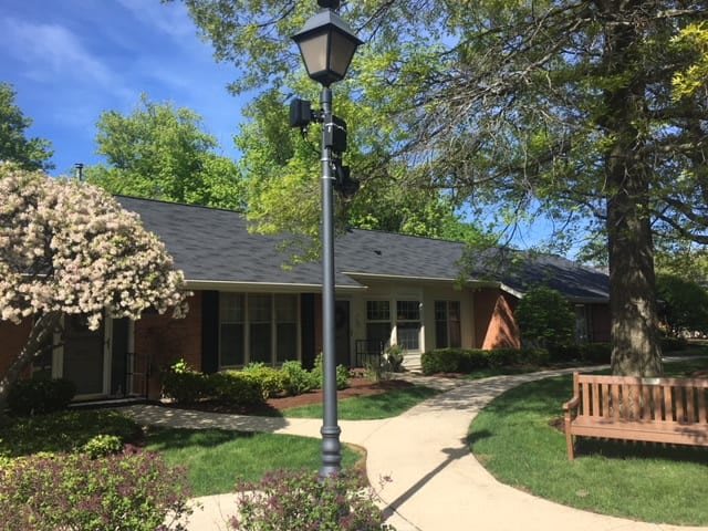 A serene view of a small building surrounded by trees and landscaping, featuring a pathway and a lamp post.