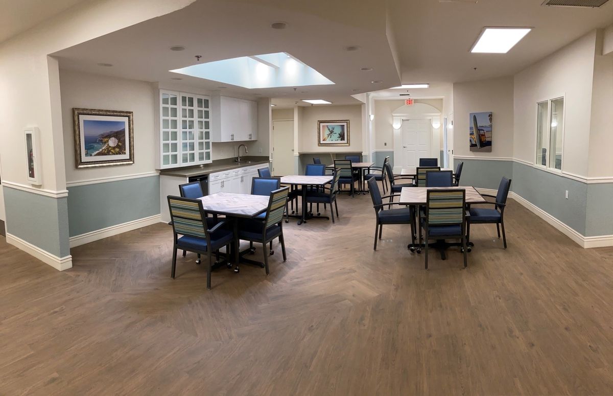 A spacious dining area with neatly arranged tables and chairs, decorated with paintings and lit by ceiling lights.
