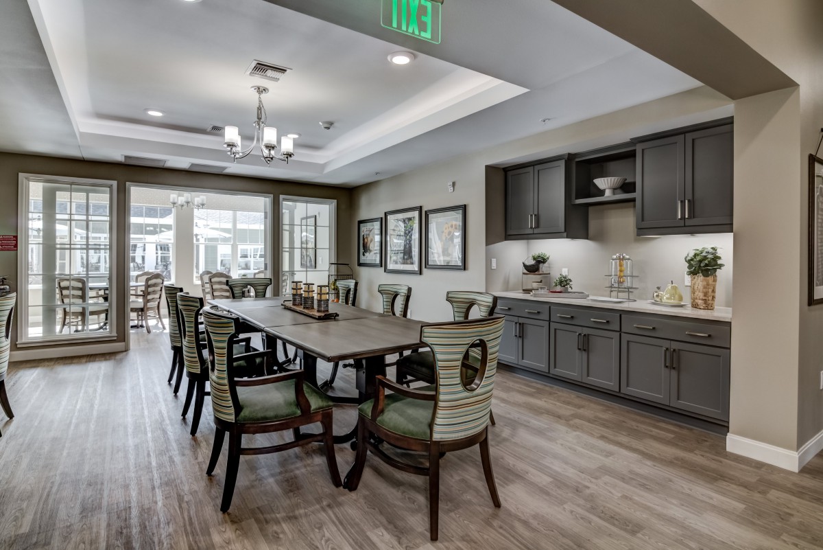A modern dining room interior with a large wooden table, stylish chairs, and a kitchen area in the background.