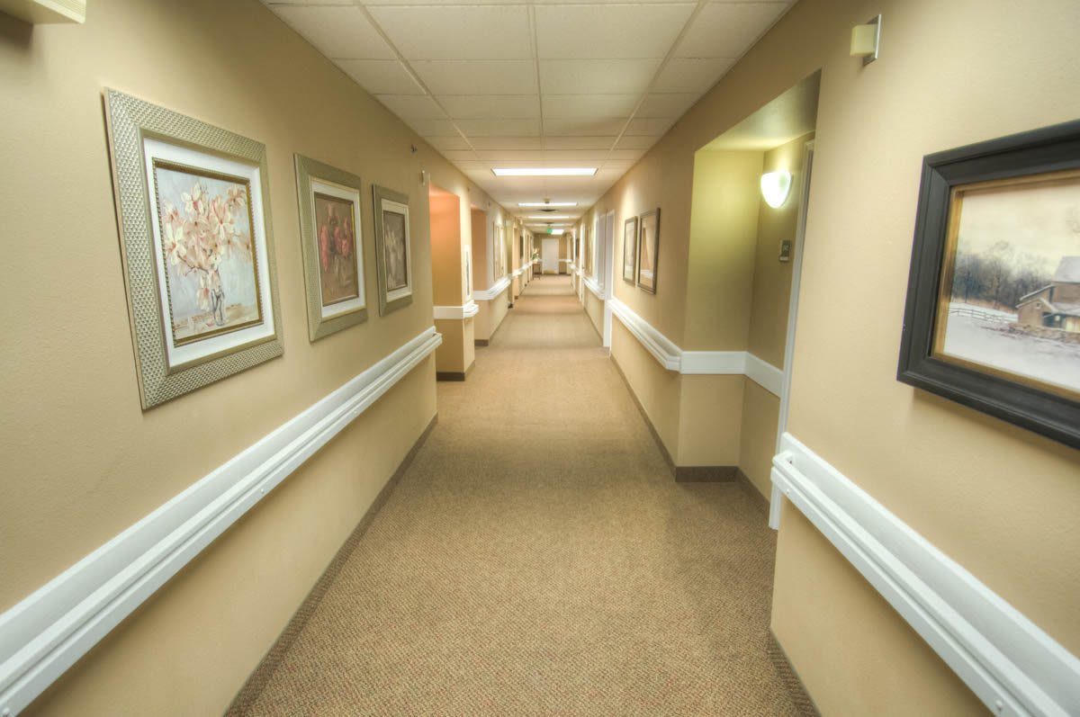 A long hospital corridor with framed artwork on the walls and bright overhead lighting.