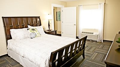 A cozy bedroom interior with a wooden bed, bedside lamp, and open door.