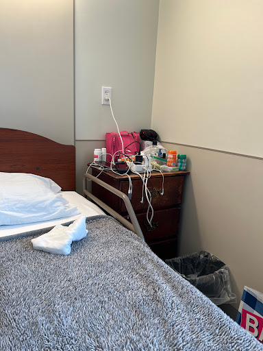 A view of a hospital patient room featuring a bed and a nightstand with various medical items.